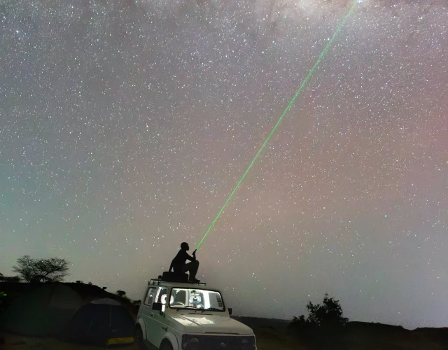 A person on a vehicle pointing a green beam into a sky full of stars