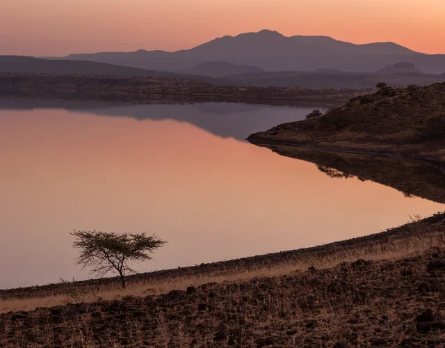 Still water reflecting hills beneath an orange sky